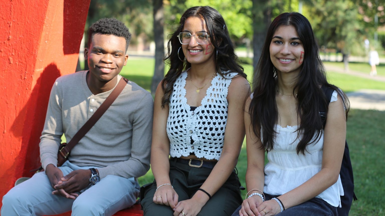 Three engineering students sit on the UBC Engineering Cairn at UBC Okanagan campus.